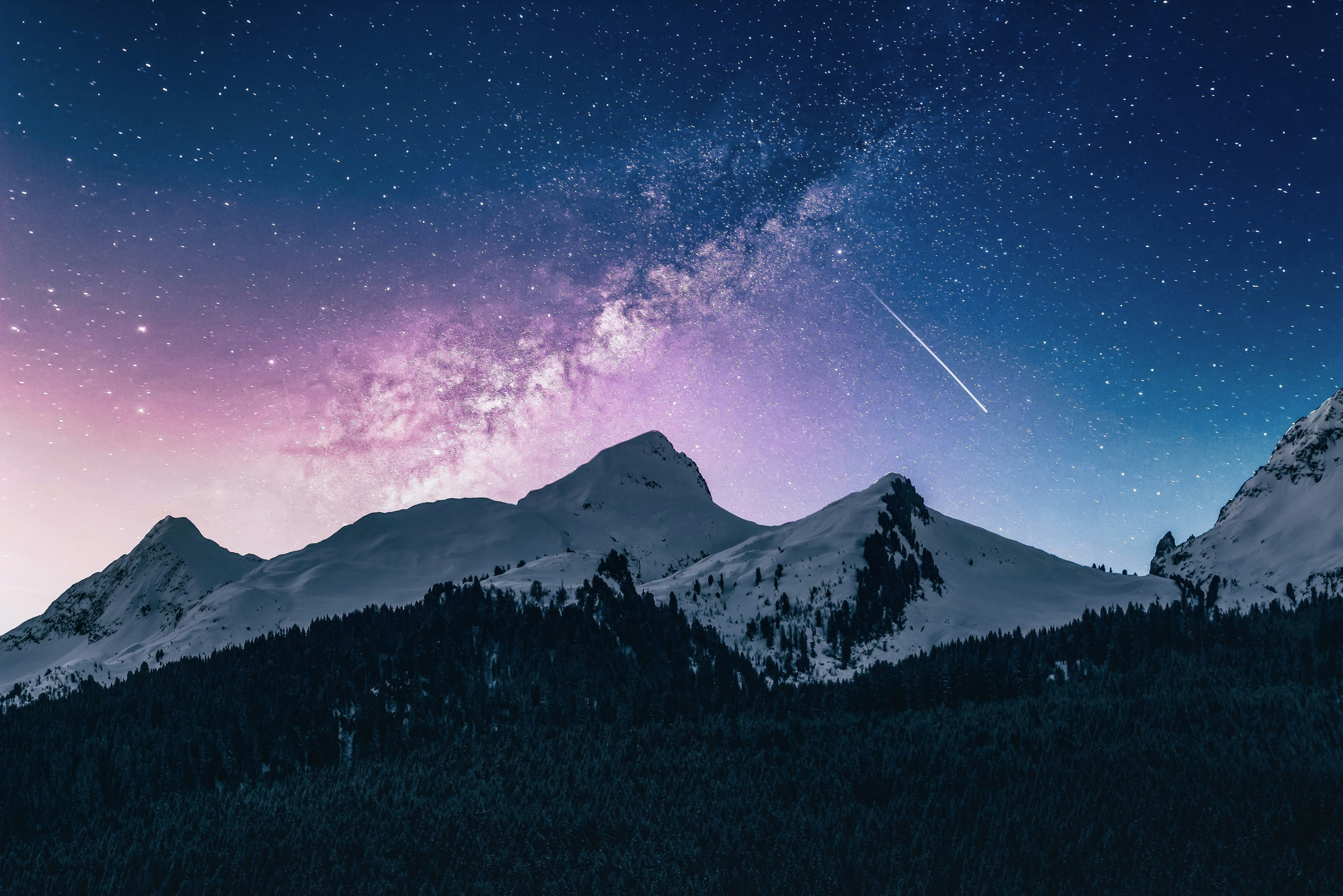A lone traveller beneath snowy mountain peaks under a night sky